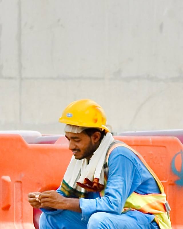 Un trabajador en su descanso, sentado en una cubeta, mirando su teléfono