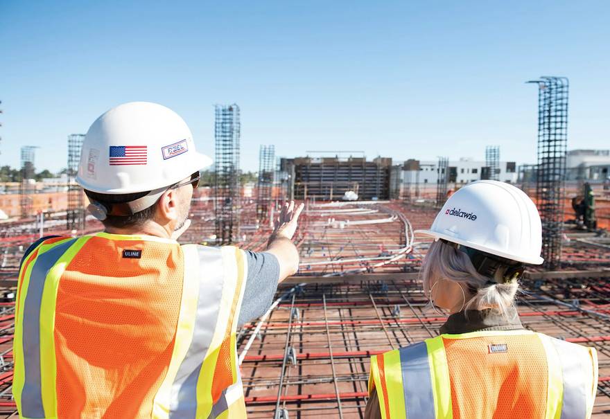 Dos trabajadores con chalecos de seguridad en una obra, uno señalándole algo al otro