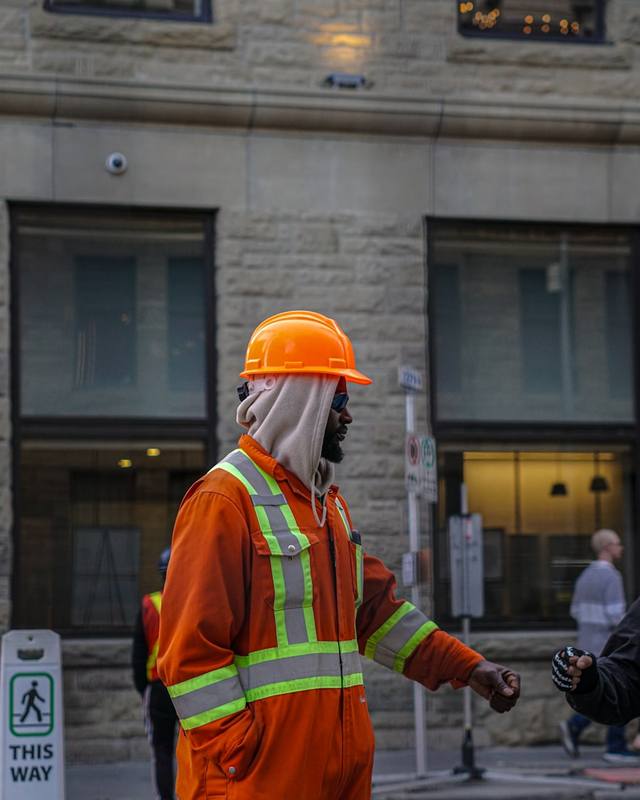 Un trabajador con overol naranja y casco en una calle de la ciudad